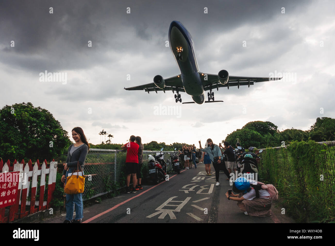 Sunset at 'Airplane Alley' - people pose for photos as an Airbus A330-300 flies low over their heads on approach to Songshan Airport, Taipei Stock Photo