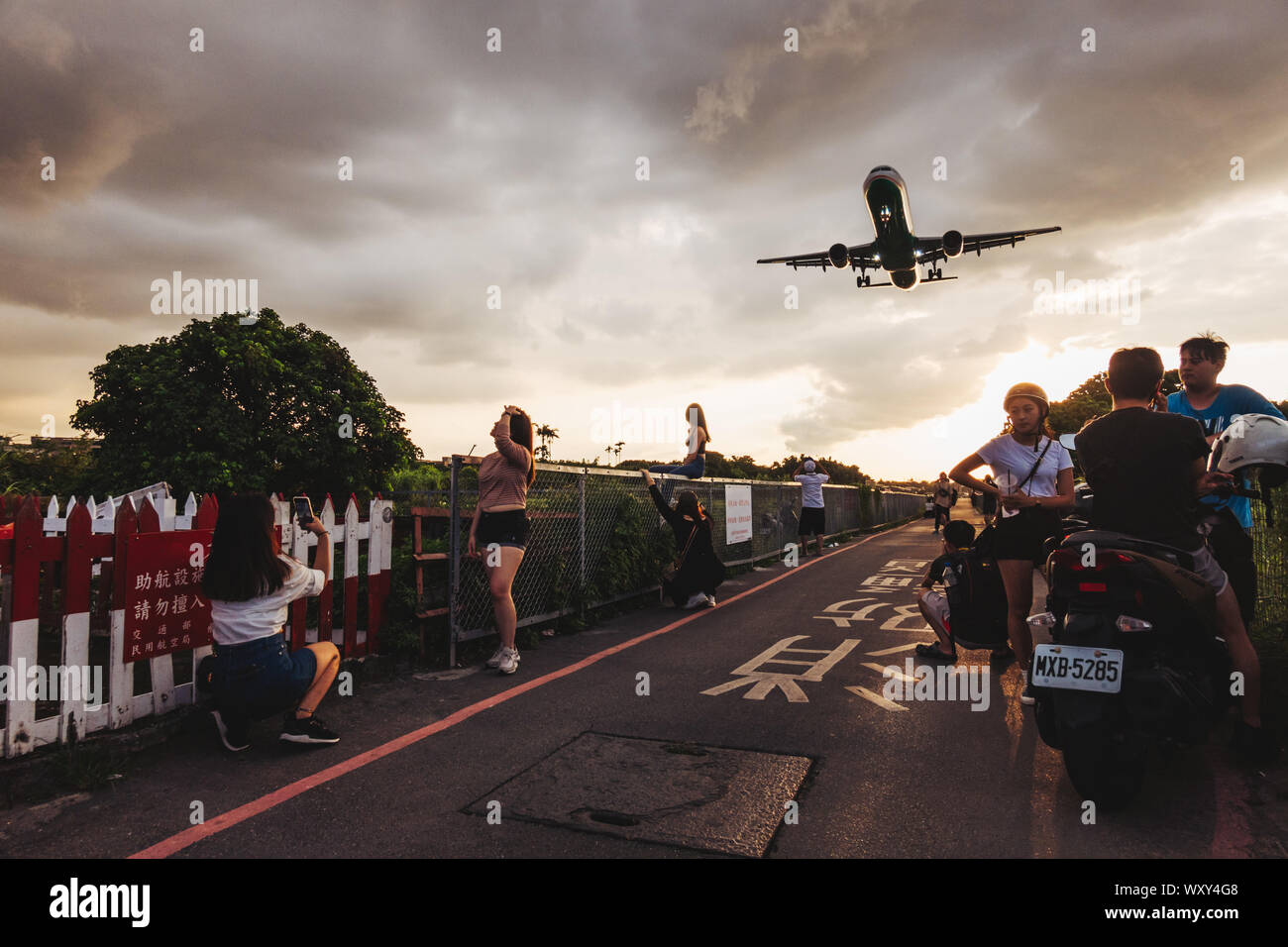 Girls pose for a photo for social media while an Airbus A321 flies low over their heads while landing at Songshan Airport, Taipei Stock Photo