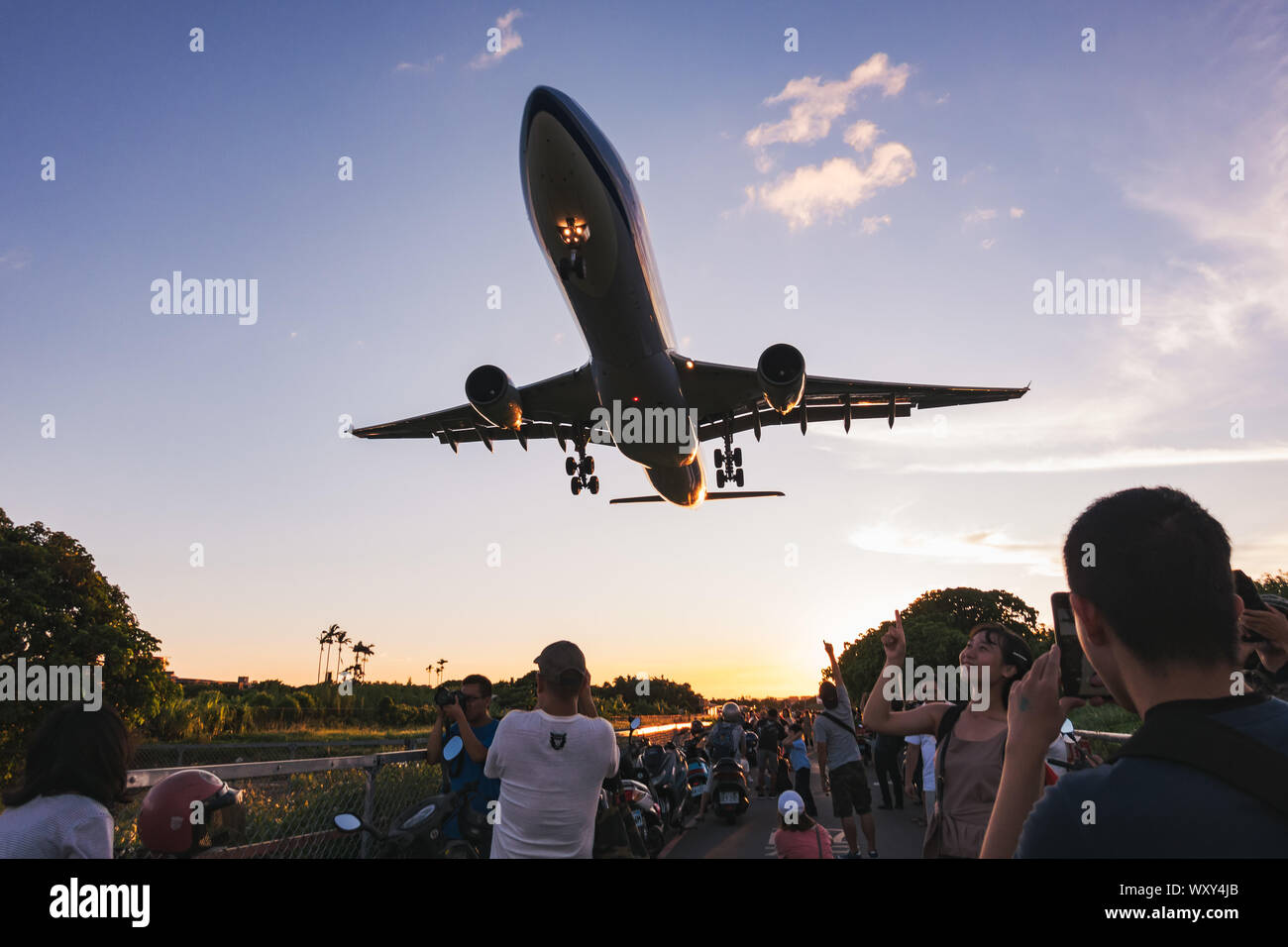 Spectators pose for photos as an Airbus A330-300 flies very low over their heads on approach to Songshan Airport, Taipei Stock Photo