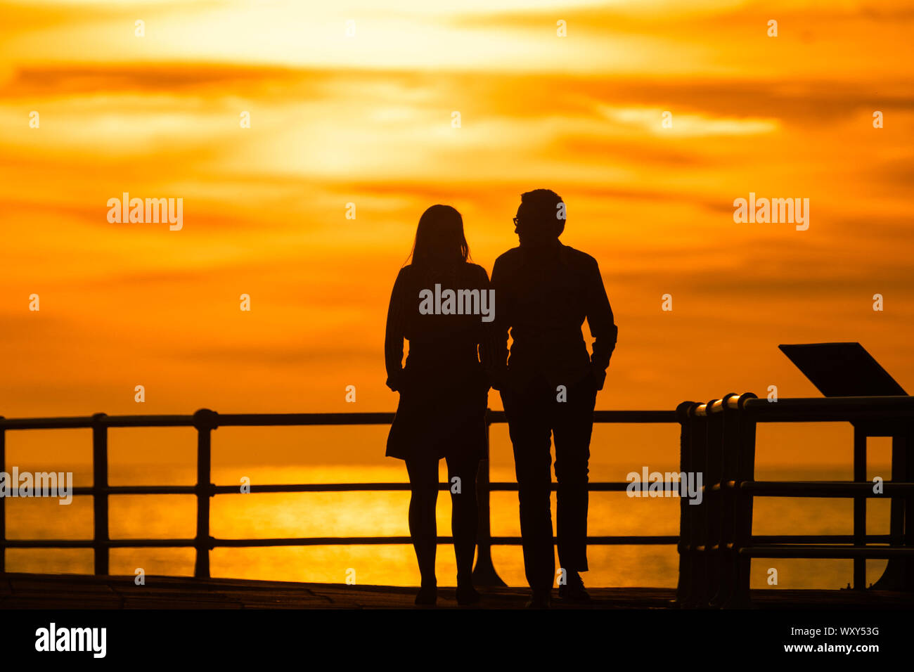 Aberystwyth, UK. 18th Sep, 2019. Aberystwyth Wales UK, Wednesday 18 September 2019 The sun setting gloriously over  Cardigan Bay silhouettes people walking along the promenade at the end of a day of unbroken clear blue skies and warm September sunshine in Aberystwyth ,  as the ‘indian summer’ mini heat-wave continues over much of the souther parts of the UK   Credit: keith morris/Alamy Live News Stock Photo