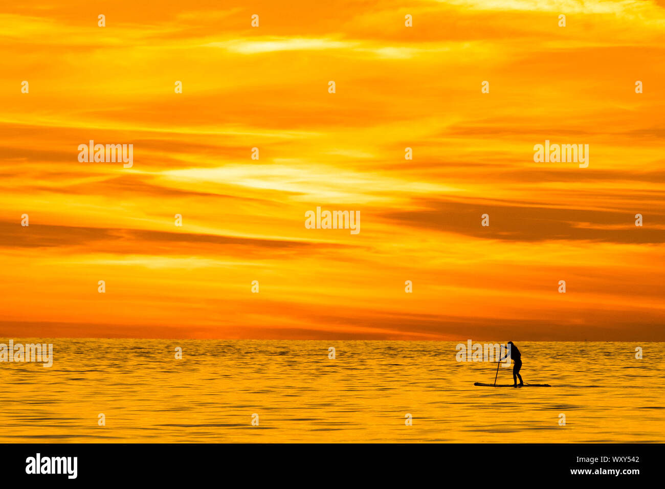 Aberystwyth, UK. 18th Sep, 2019. Aberystwyth Wales UK, Wednesday 18 September 2019 The sun setting gloriously over  Cardigan Bay silhouettes a person paddle-boarding on the calm sea the end of a day of unbroken clear blue skies and warm September sunshine in Aberystwyth ,  as the ‘indian summer’ mini heat-wave continues over much of the souther parts of the UK   Credit: keith morris/Alamy Live News Stock Photo