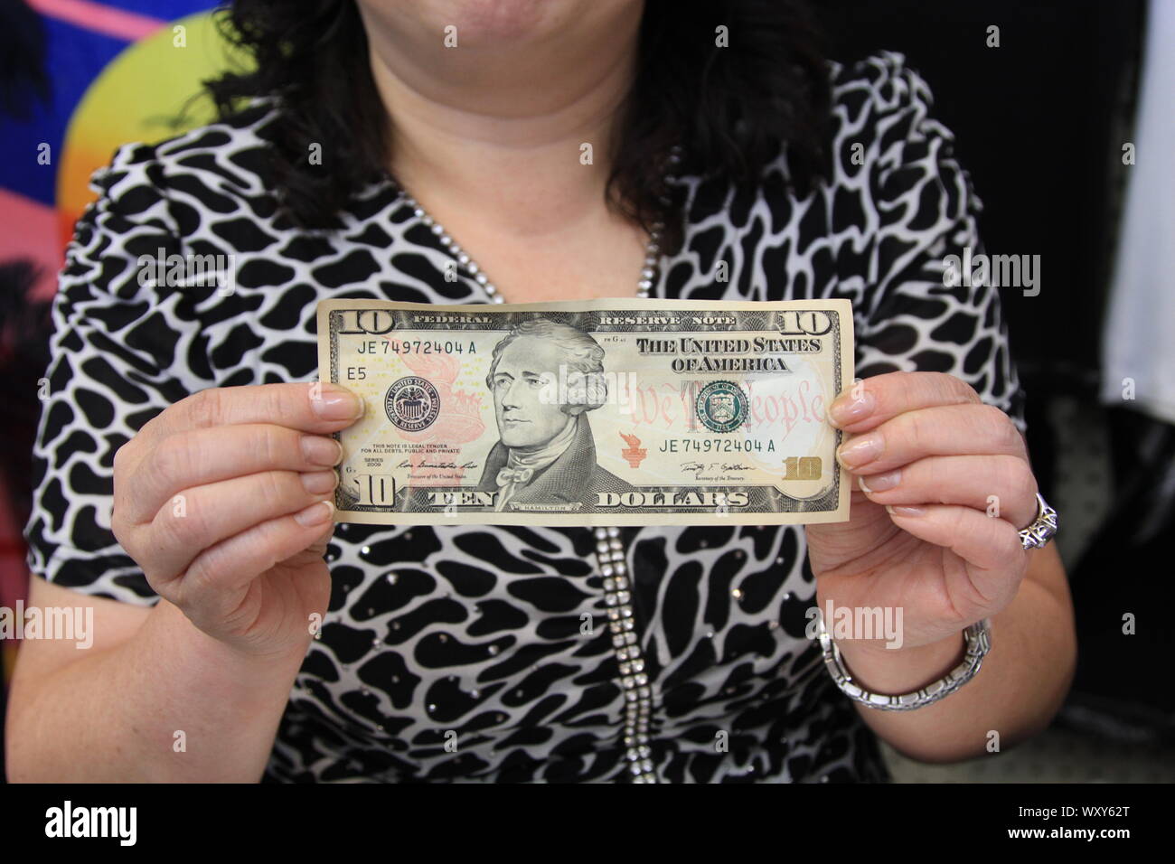 A WOMAN HOLDING A $10 DOLLAR NOTE. MONEY. CURRENCY. WORLD CURRECIES. THE US DOLLAR. DOLLARS. ECONOMY. ECONOMICAL. ECONOMICS. CASH. PAPER MONEY. CASH SOCIETY. CASHLESS SOCIETY. WONGA. DOSH. GREEN BACK. FEMALE HOLDING MONEY. POCKET MONEY. POVERTY. CHILD POVERTY. BILL. BILLS. TEN DOLLAR BILL. Girl Boss. Women entrepreneurs. Stock Photo