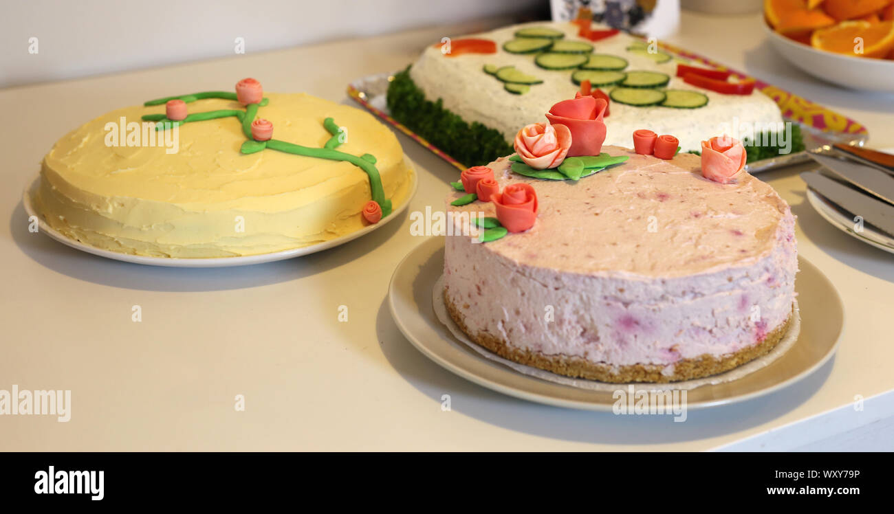 Multiple cakes on a table. There is home made yellow orange & chocolate cake with butter cream frosting, pink berry cake and a Scandi sandwich cake. Stock Photo