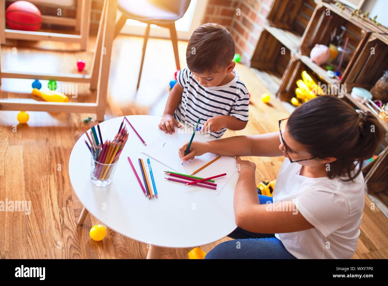 Beautiful teacher and toddler boy drawing draw using colored pencils at ...