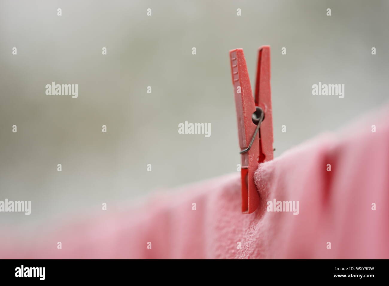 Red clothespin holds clothes on a rope, macro image. Stock Photo