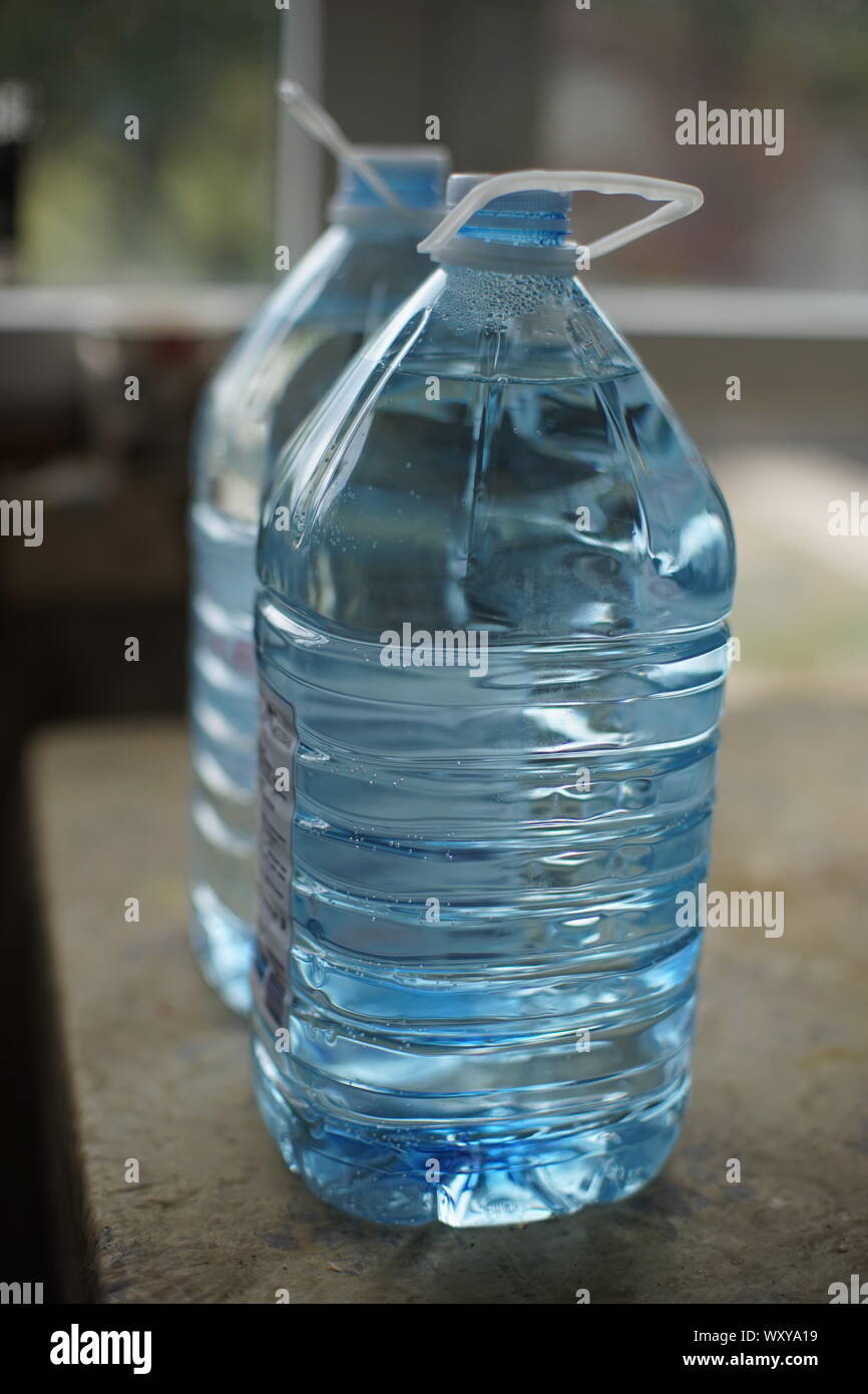Two five-liter plastic bottles full of water on the table, side  Stock Photo