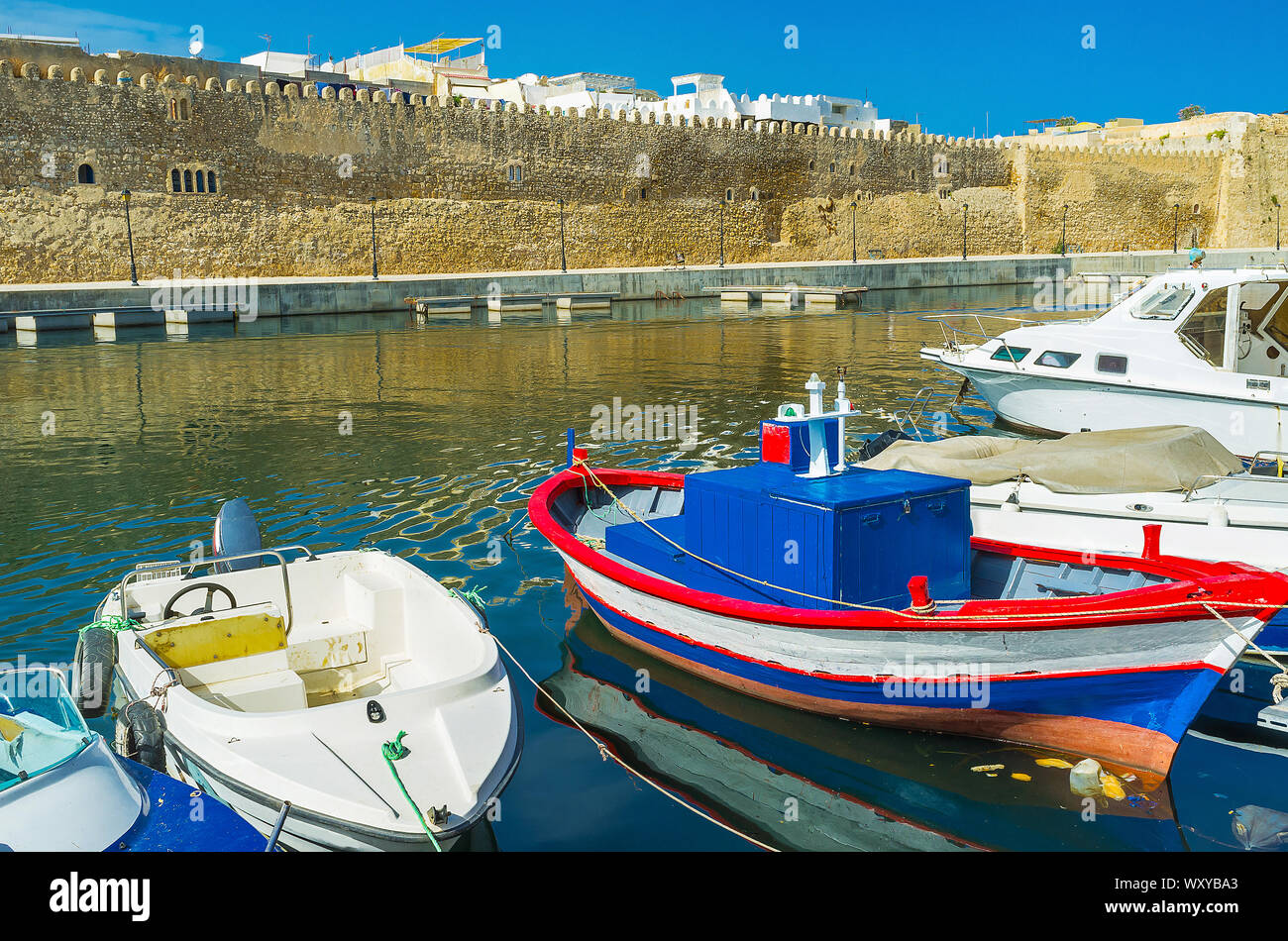 The view on colorful fishing boats, moored in port, and the medieval wall of Kasbah fortress on the background, Bizerte, Tunisia Stock Photo