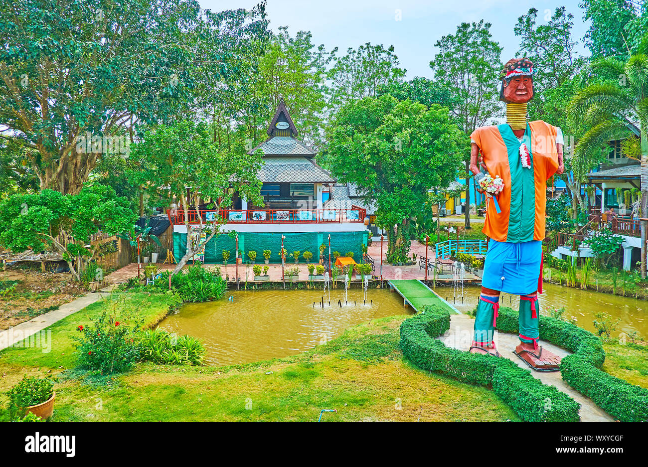 PAI, THAILAND - MAY 5, 2019: The metal statue of Karen tribe long neck woman in colorful clothes, standing among the small ponds in park of the countr Stock Photo