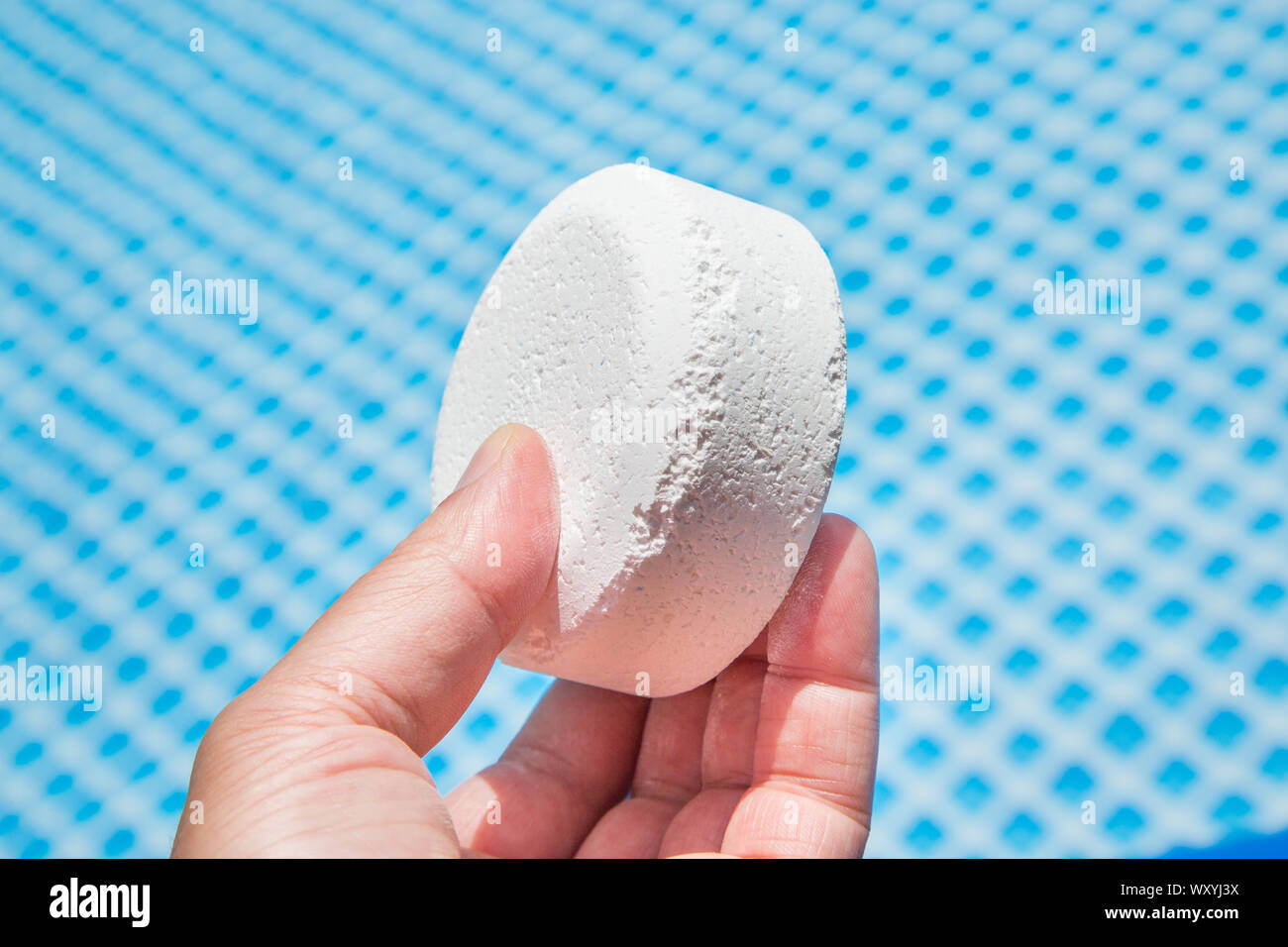 Hand holding Chlorine Pellets with inflatable pool on background Stock