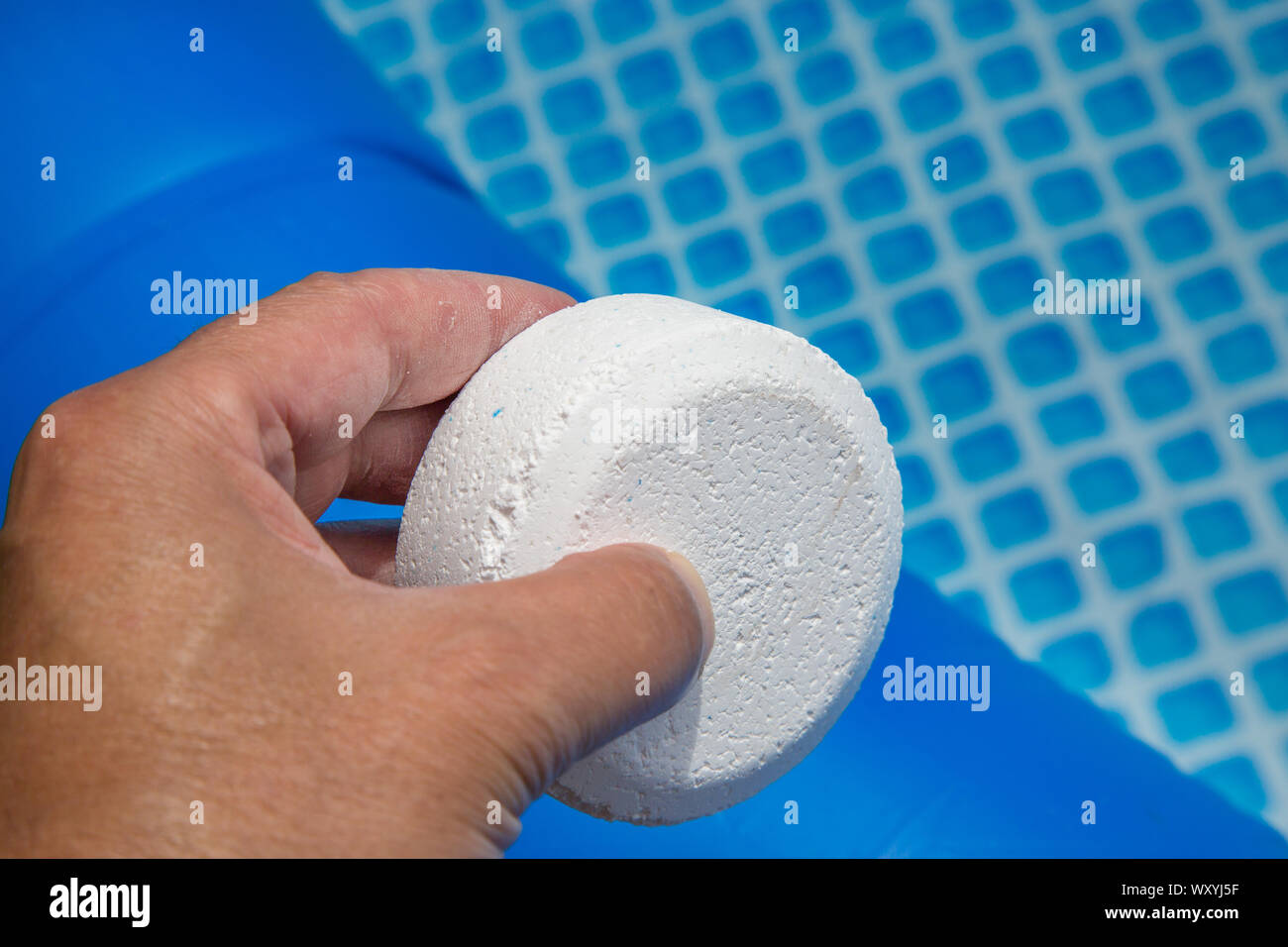 Hand holding Chlorine Pellets with inflatable pool on background Stock