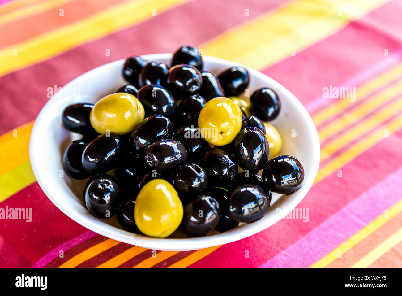 Green and black olives in a bowl on a colourful striped tablecloth Stock Photo