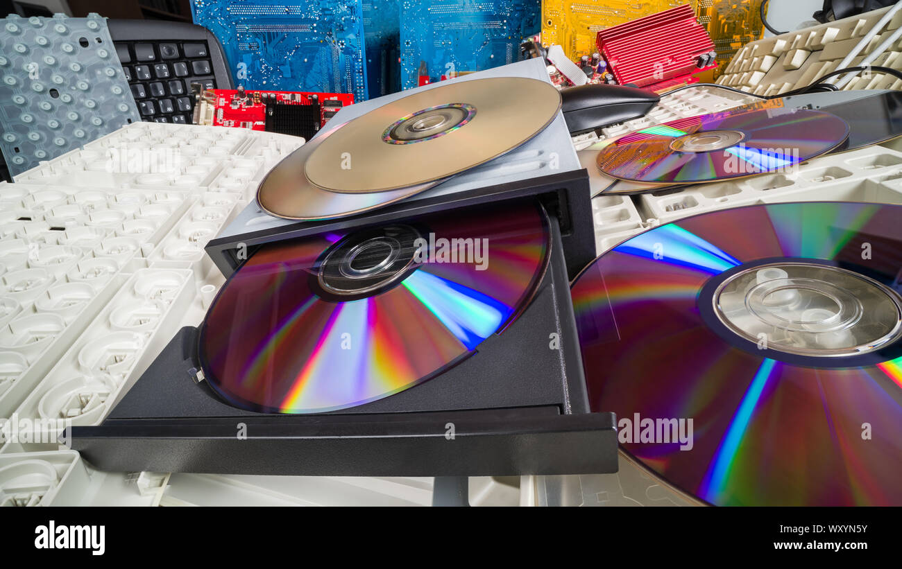 Compact discs and keyboards in a heap of old computer parts. E-waste sorting and recycling. Obsolete digital data storage device in CD drive. Ecology. Stock Photo