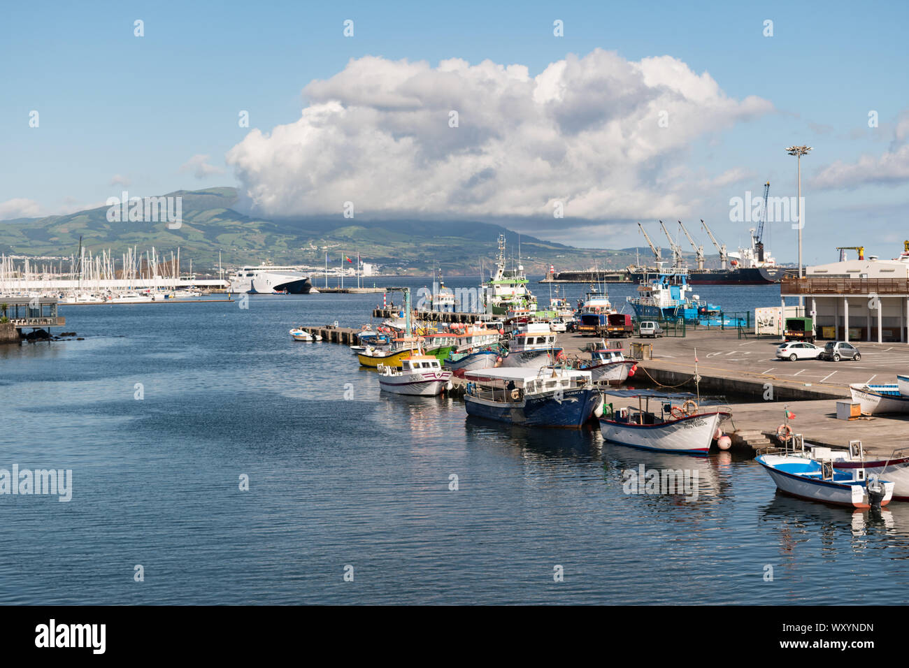 Boats moored in the harbour of Ponta Delgada on São Miguel Island with a large cloud sitting above the island's volcanic hillside on a bright day. Stock Photo