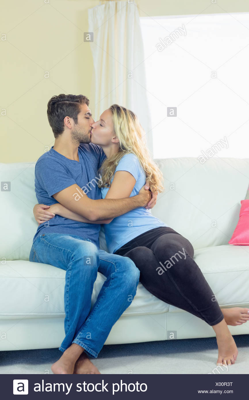 Sweet Young Couple Sitting Kissing On A Couch Stock Photo
