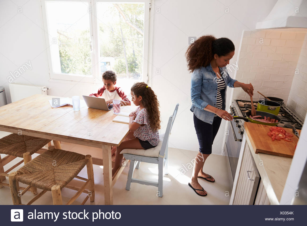 Mum Cooking While Kids Work At Kitchen Table