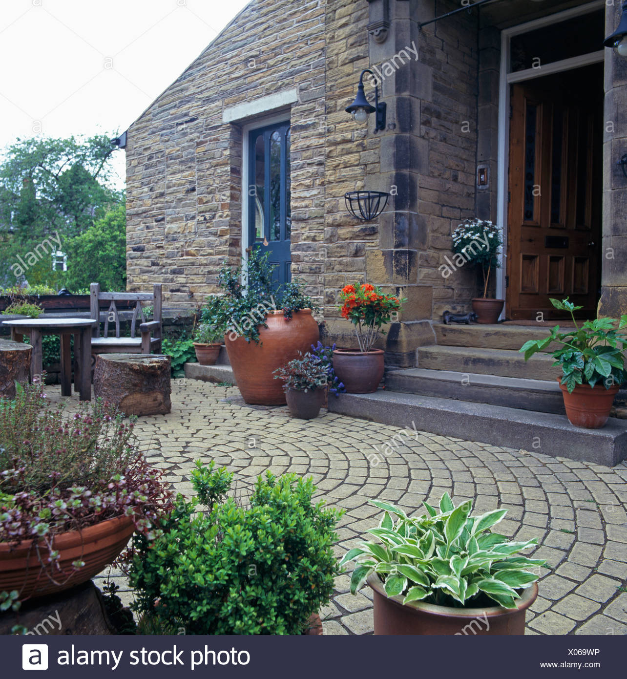Pots Of Perennials And Small Shrubs On Circular Paved Patio In
