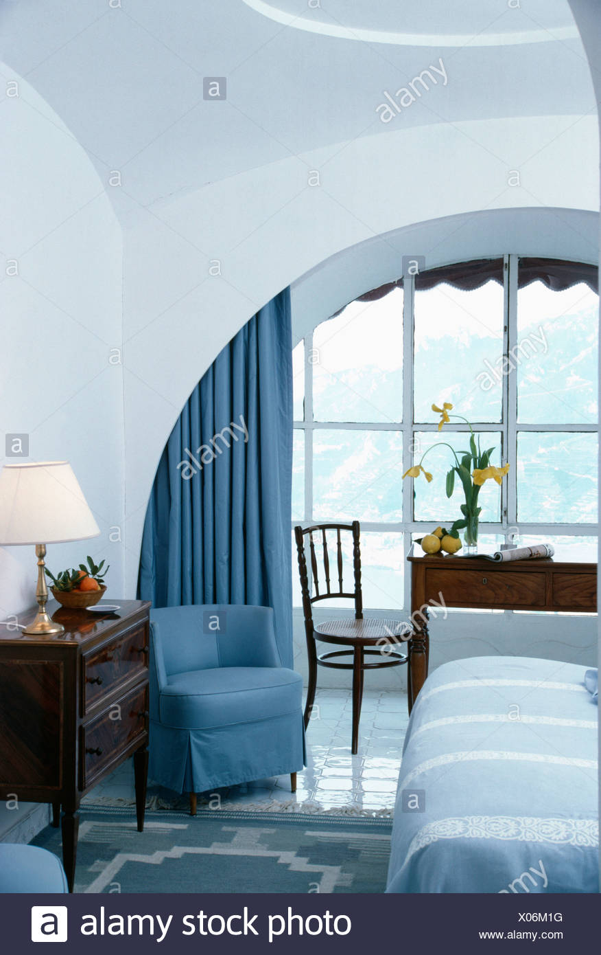 Modern Bedroom With Blue Chair And Drapes And Arched Window Alcove