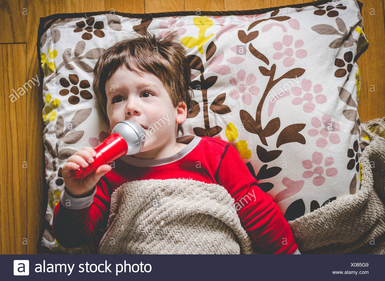 Little Boy Lying On The Floor Singing Into A Toy Microphone Stock