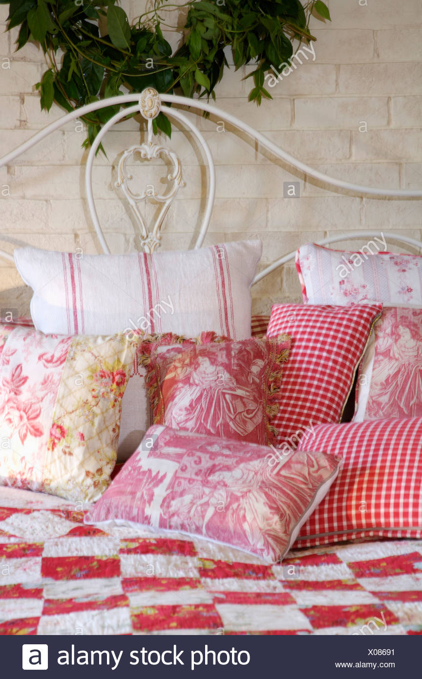 White Metal Bed With Pink White Checked And Floral Cushions Piled On Red White Patchwork Quilt Stock Photo Alamy
