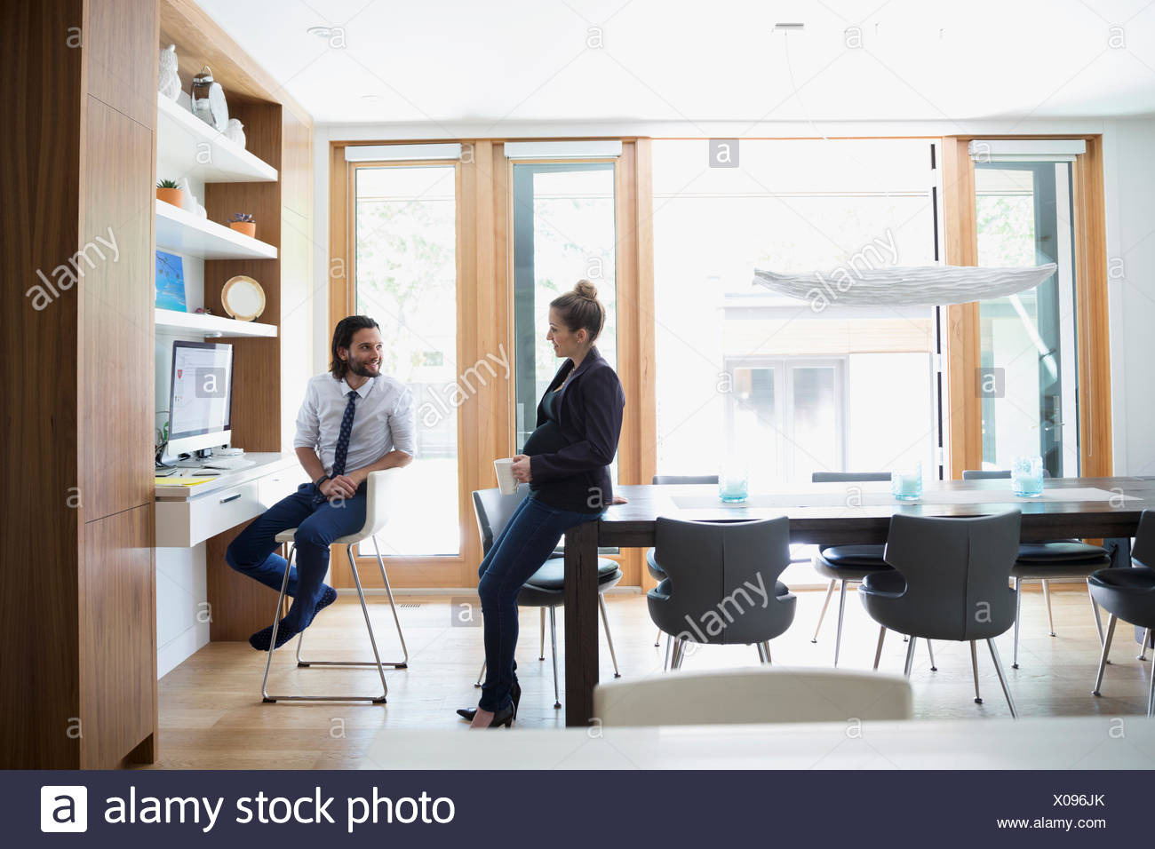 Pregnant Couple Talking At Computer Desk In Dining Room Stock