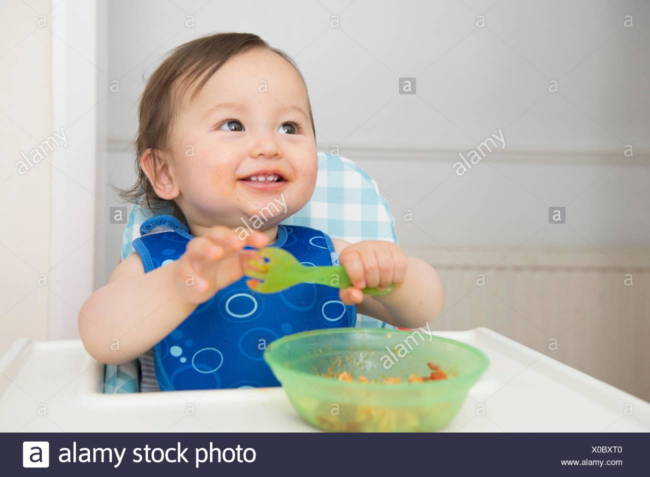 Baby Boy Eating Baby Food In Kitchen High Chair Stock Photo
