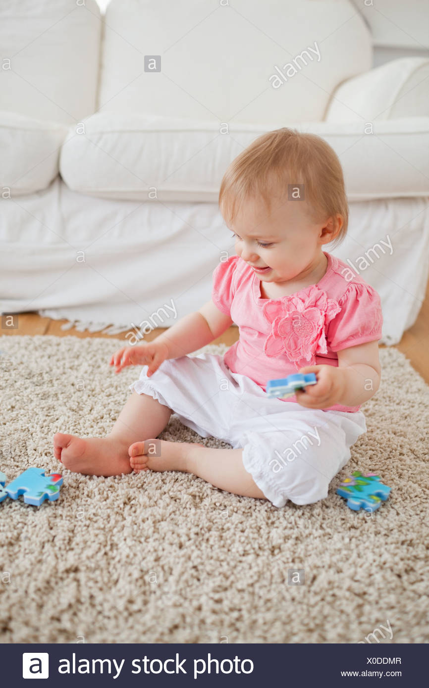 Baby Playing With Puzzle Pieces While Sitting On A Carpet Stock