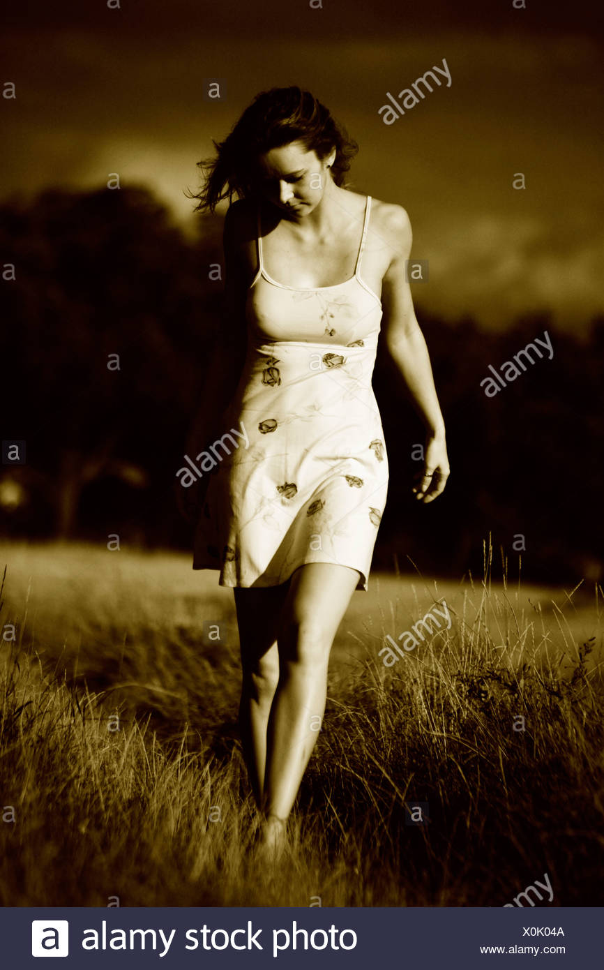 Woman wearing a light summer dress, walking barefooted through a field, imminent thunder clouds in the back Stock Photo