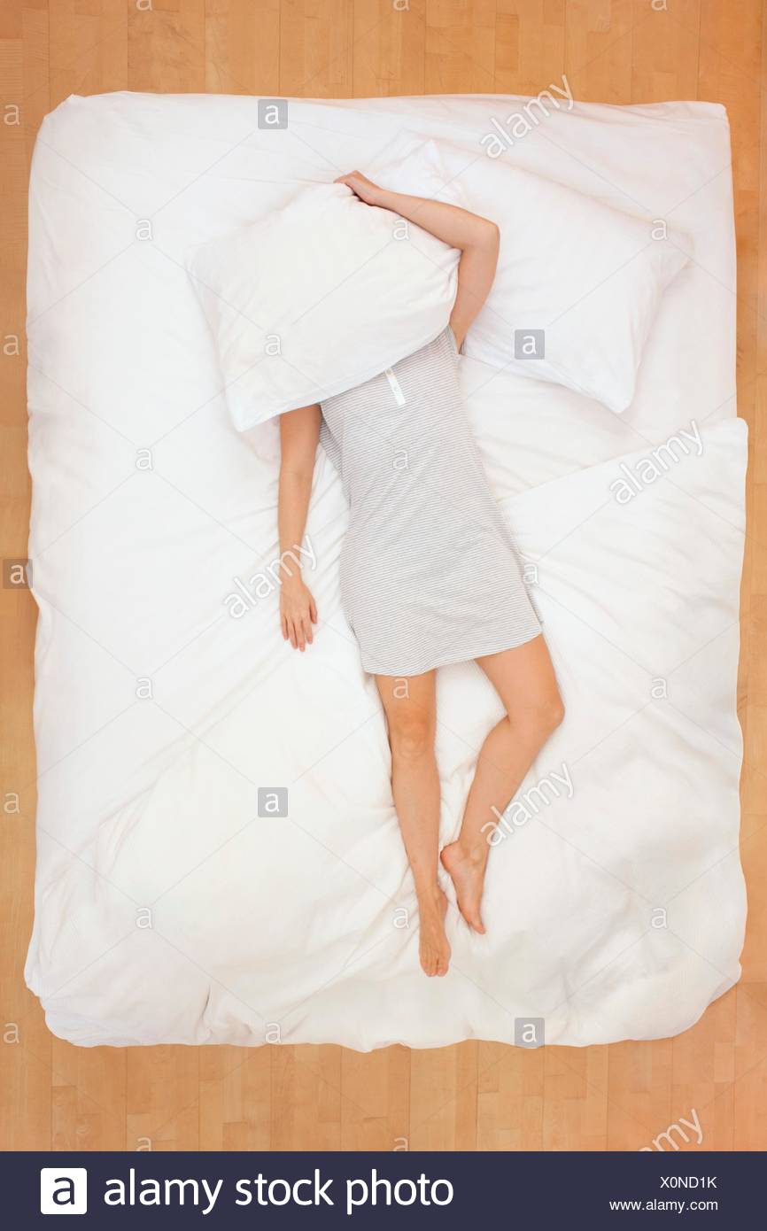 Mid Adult Woman Lying In Bed With Pillow Over Head Stock Photo