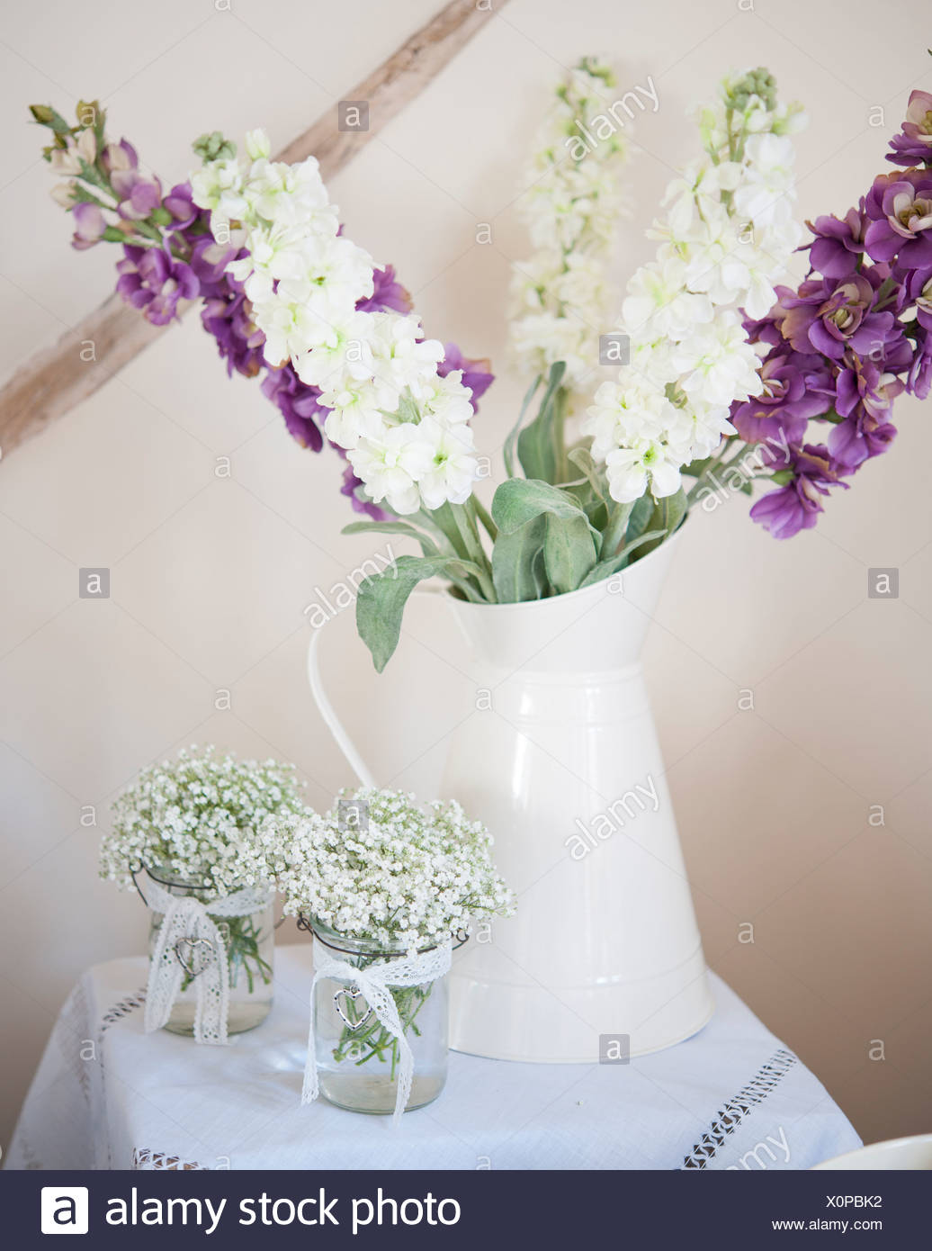 A Jug Of Purple And White Flowers With Two Small Vases Of White