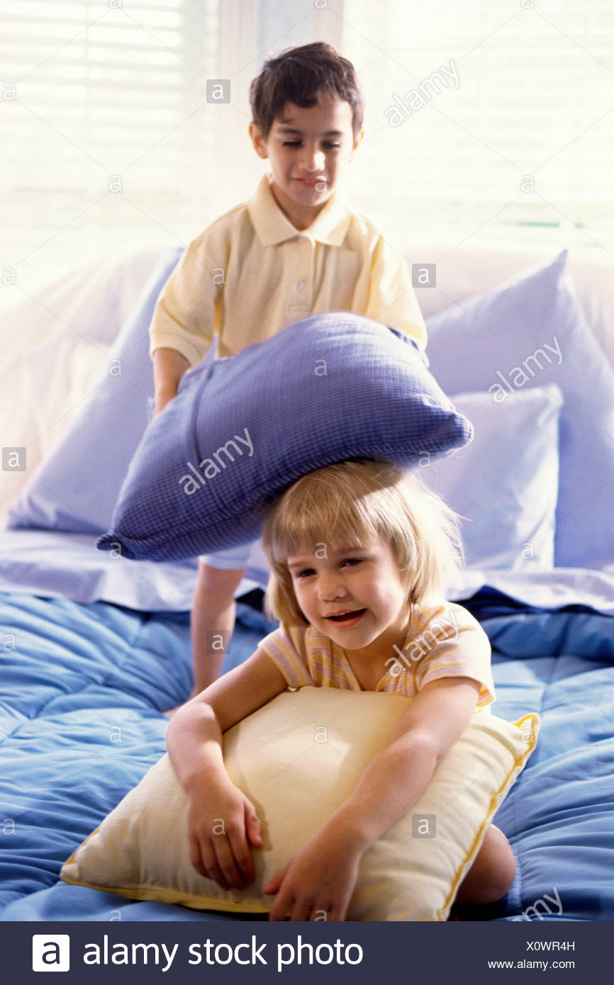Brother And Sister Having A Pillow Fight On The Bed Stock Photo