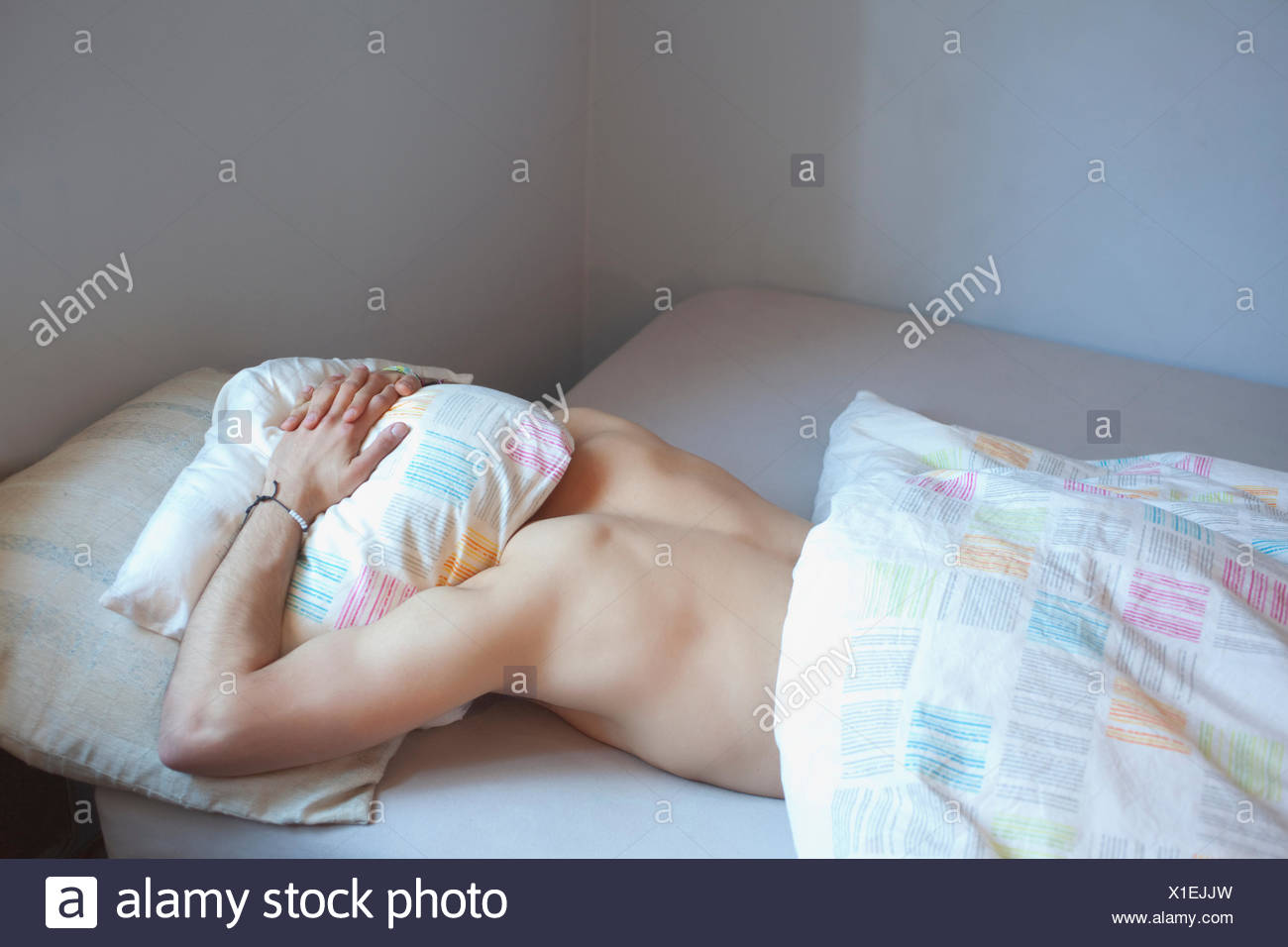 Young Man Sleeping With Head Under Pillow In Bed Stock Photo