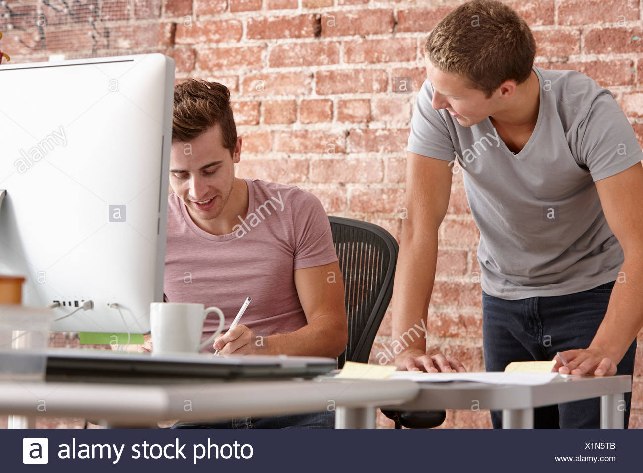 Young men talking at desk with computer Stock Photo