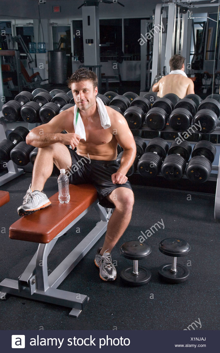 Young Man Resting On Weight Bench After Workout In Gym Next To