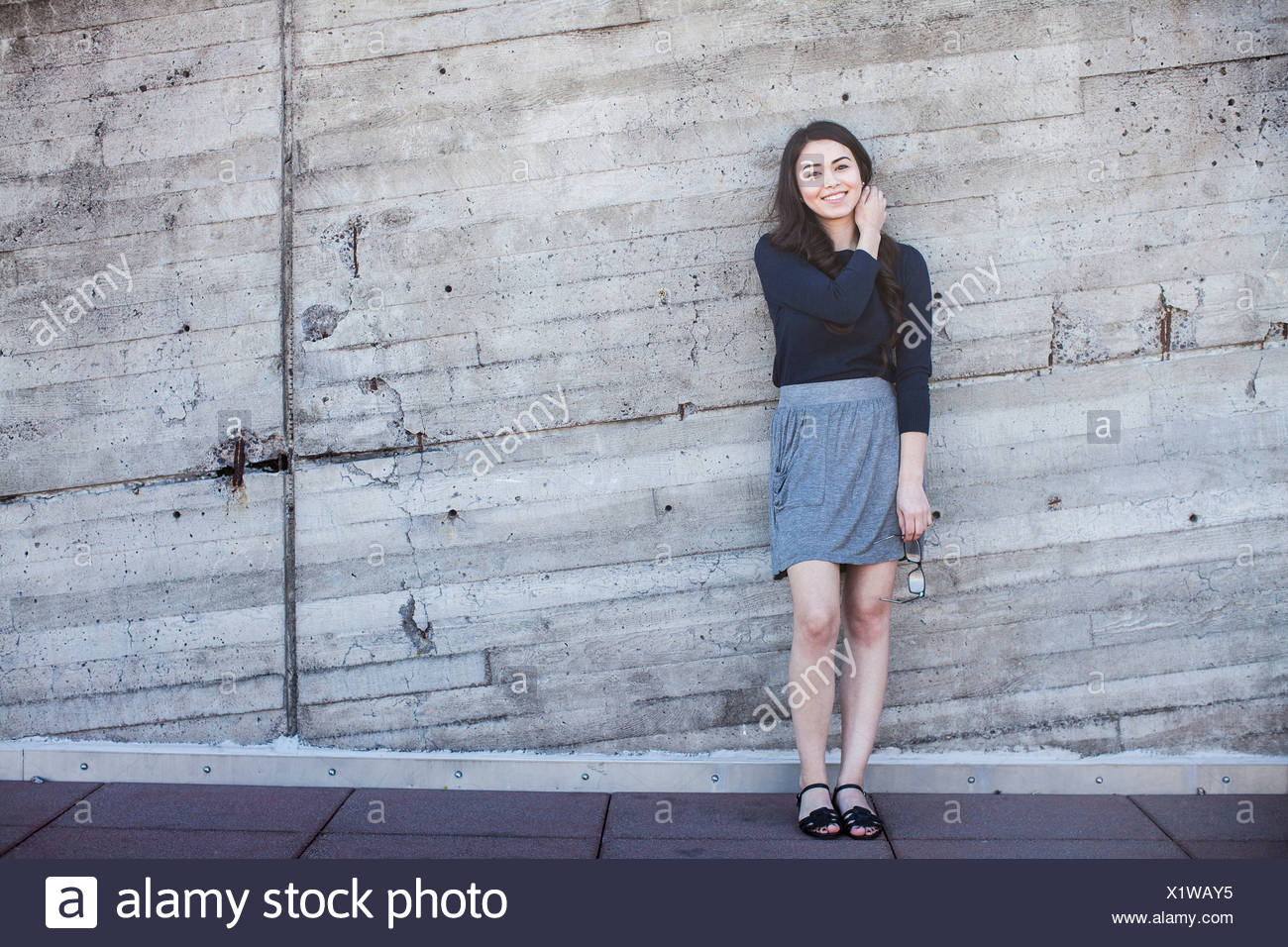 Young woman standing, leaning against wall Stock Photo