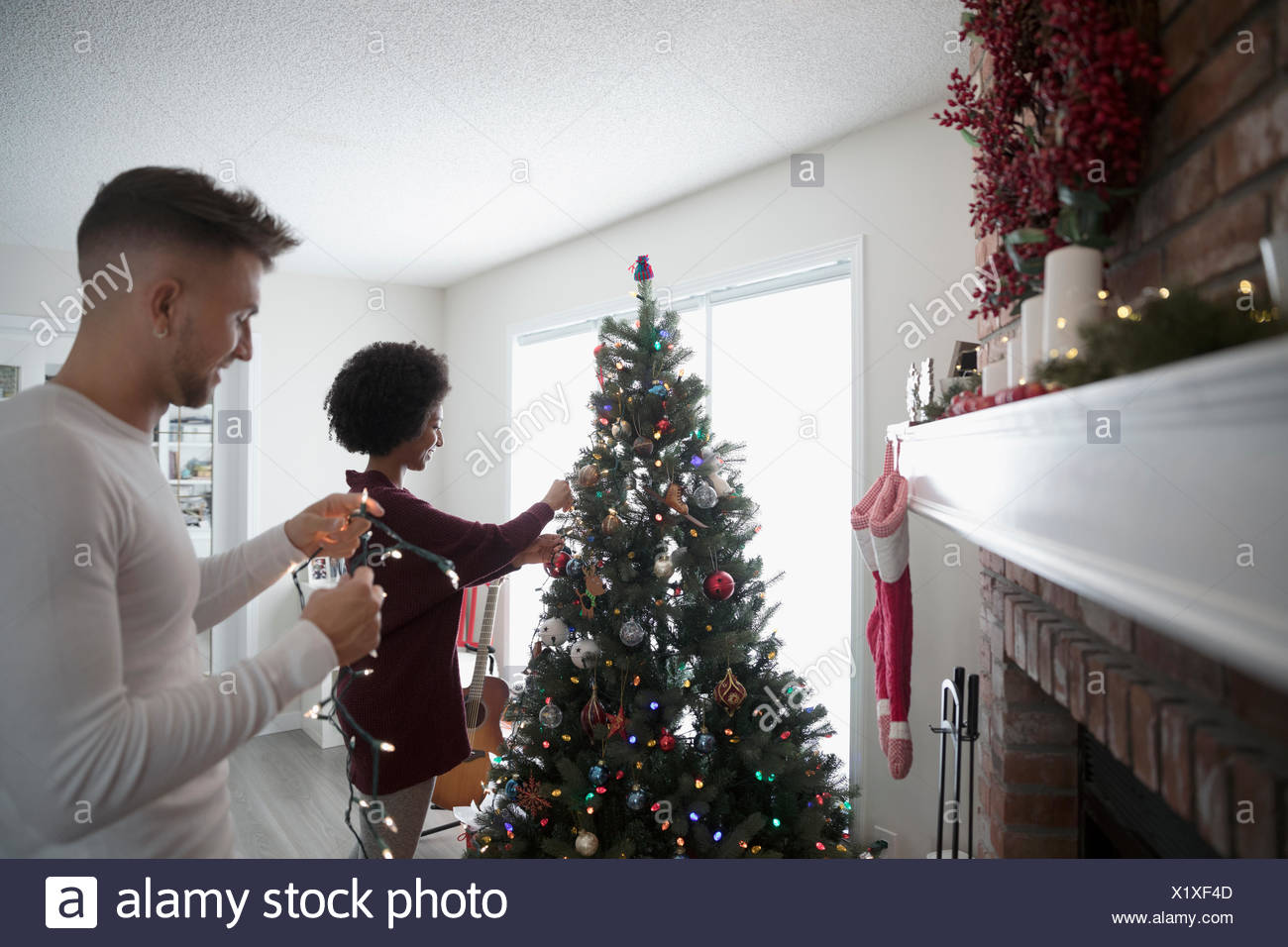 Young Couple Decorating Hanging Christmas Lights On Tree In