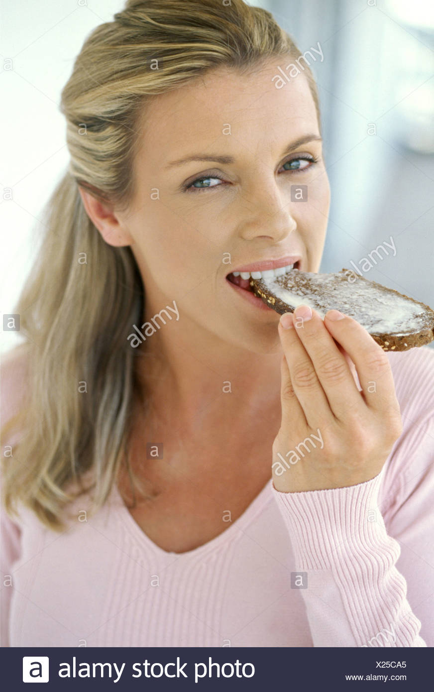 Female With Long Blonde Hair Off Face Eating Slice Of Toast With