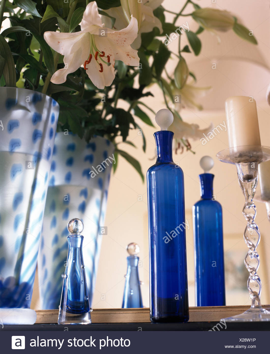 White Lilies In Blue Glass Vase On Table With Tall Blue Glass Bottles And A Clear Glass Candlestick Stock Photo Alamy