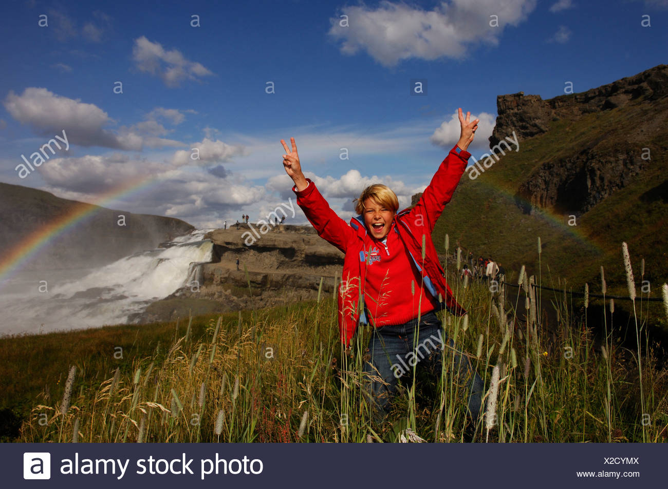 Child jubilating under rainbow on Gullfoss, The Golden Waterfall, Iceland, Europe Stock Photo