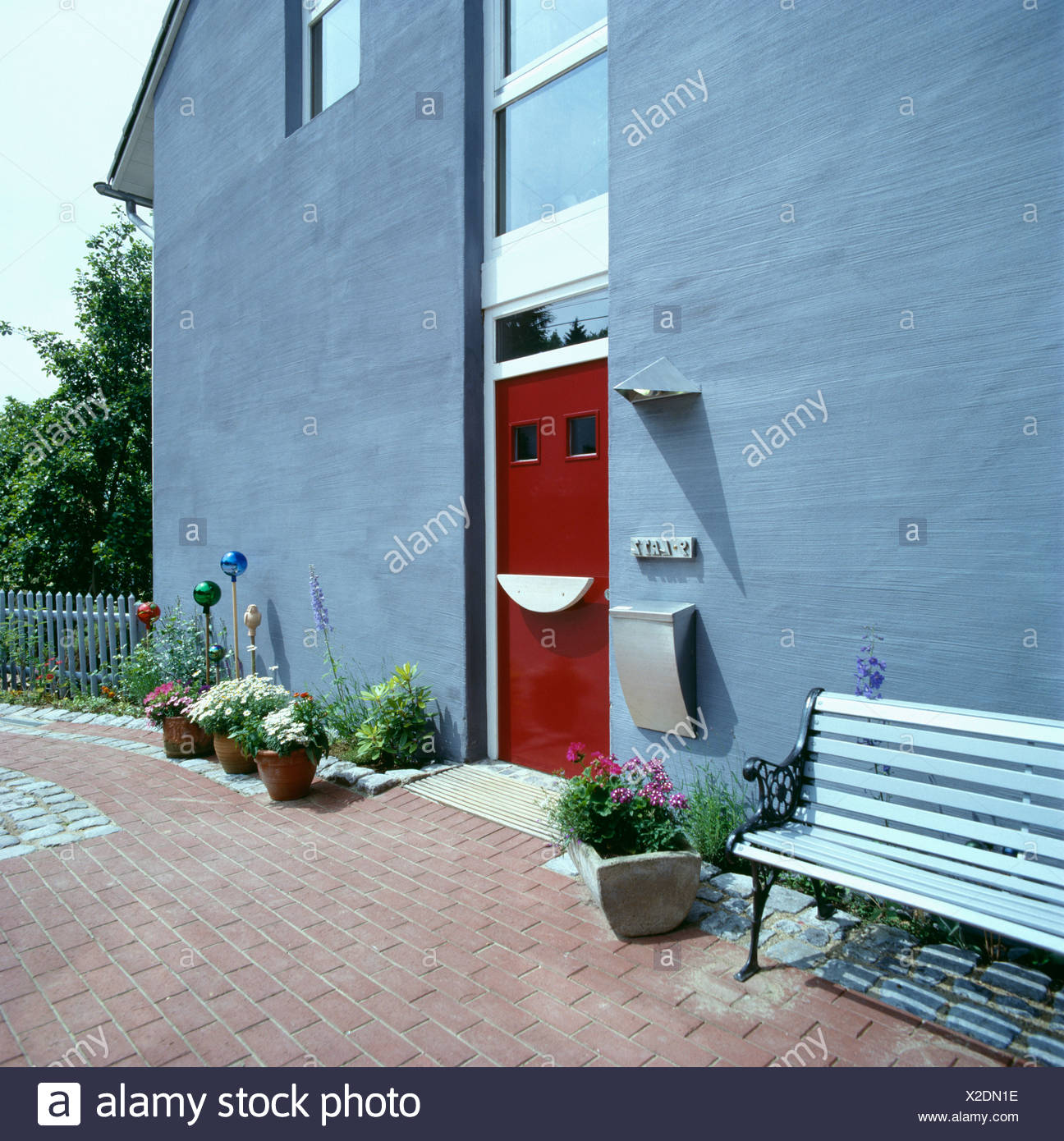 Modern Grey House With Red Front Door And Bench On Brick