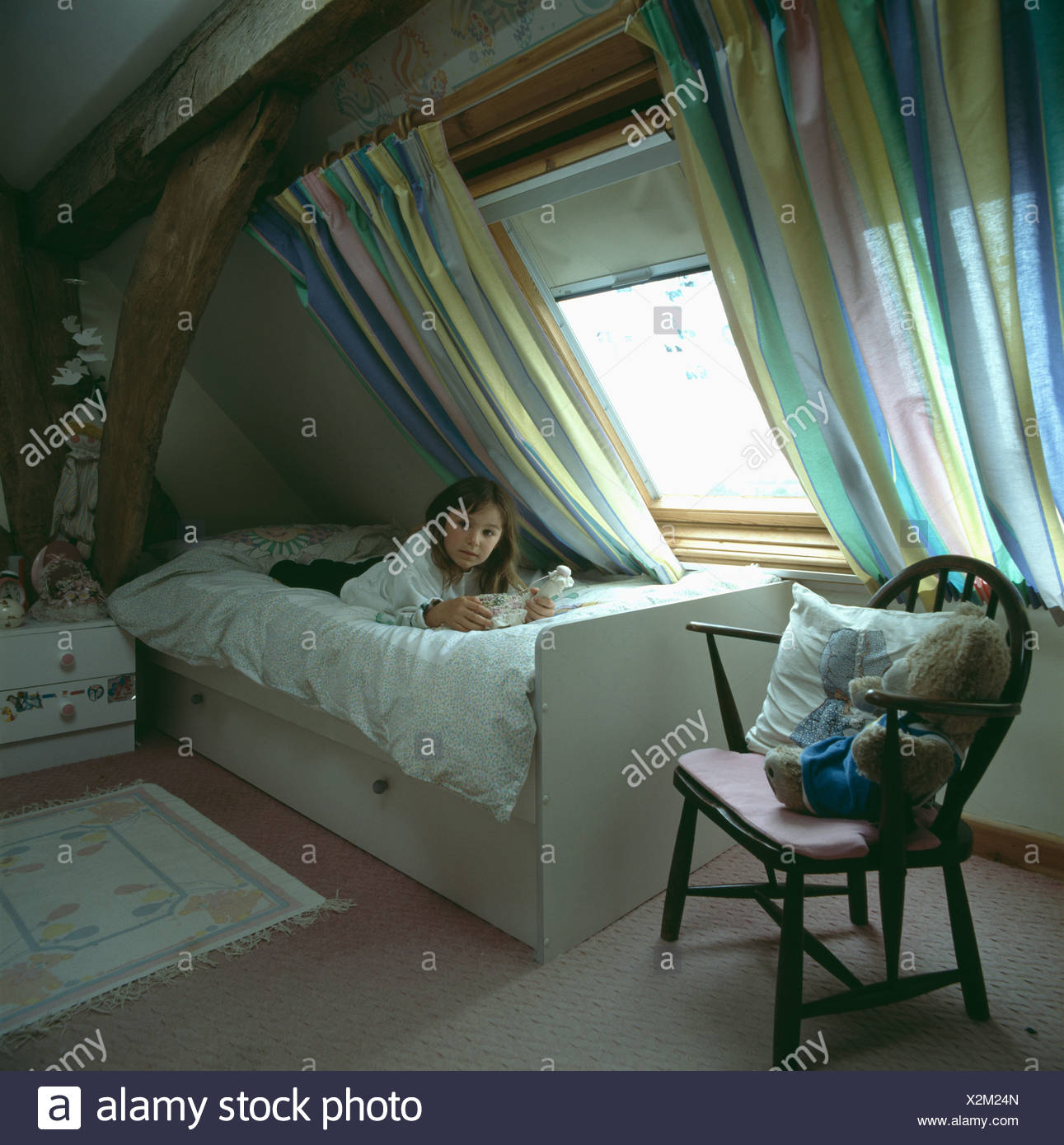 Small Girl Lying On Bed And Reading Below Window With Striped
