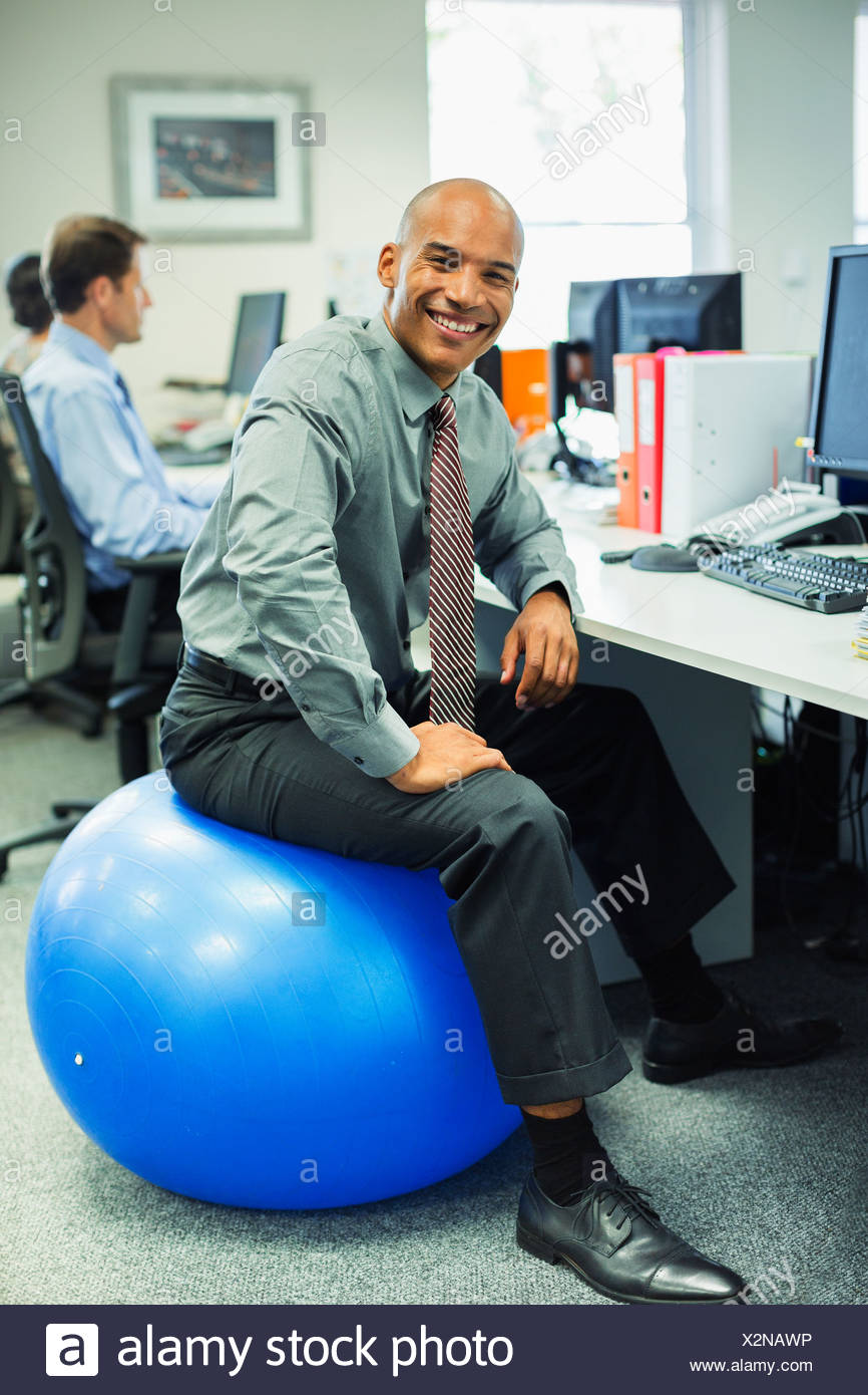 Businessman Sitting On Fitness Ball In Office Stock Photo