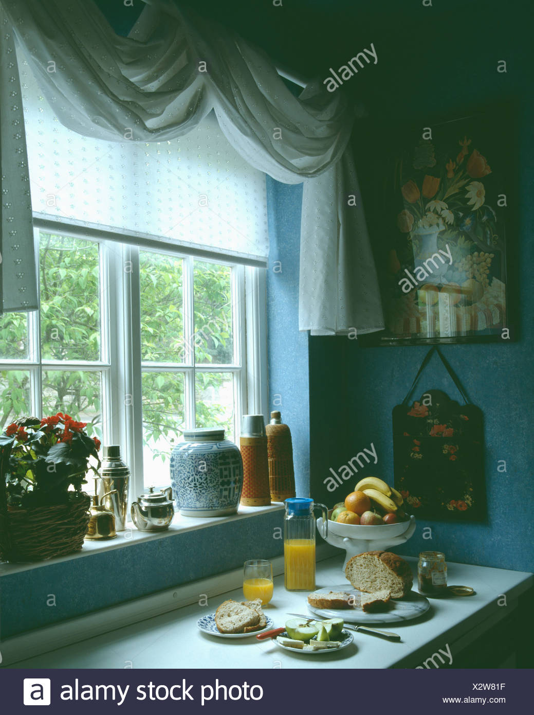 Bowl Of Fruit And Glass Of Orange On Table Below Window With White
