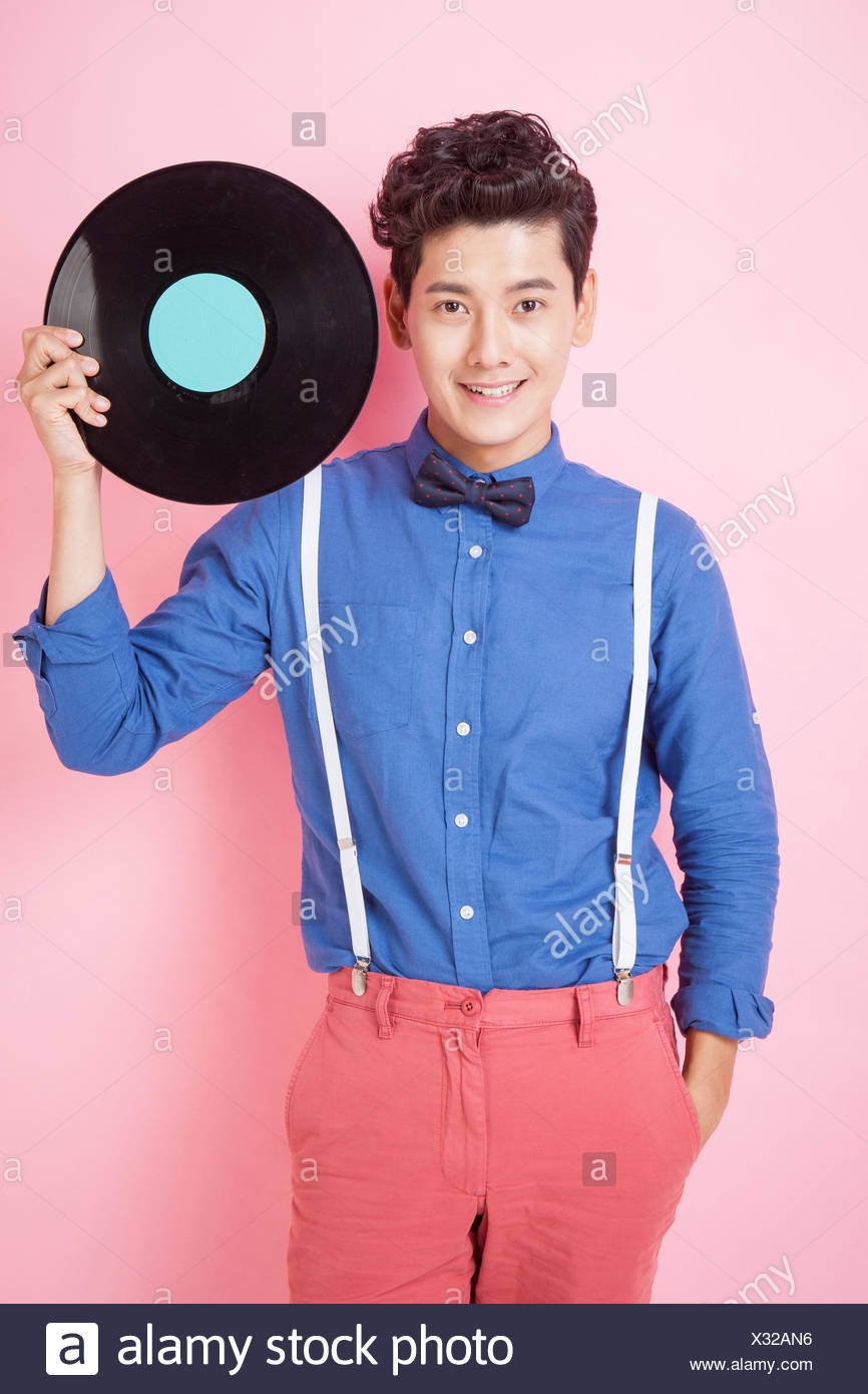 young-smiling-man-in-retro-style-holding-a-record-with-one-hand-in-his-pocket-staring-at-front-X32AN6.jpg