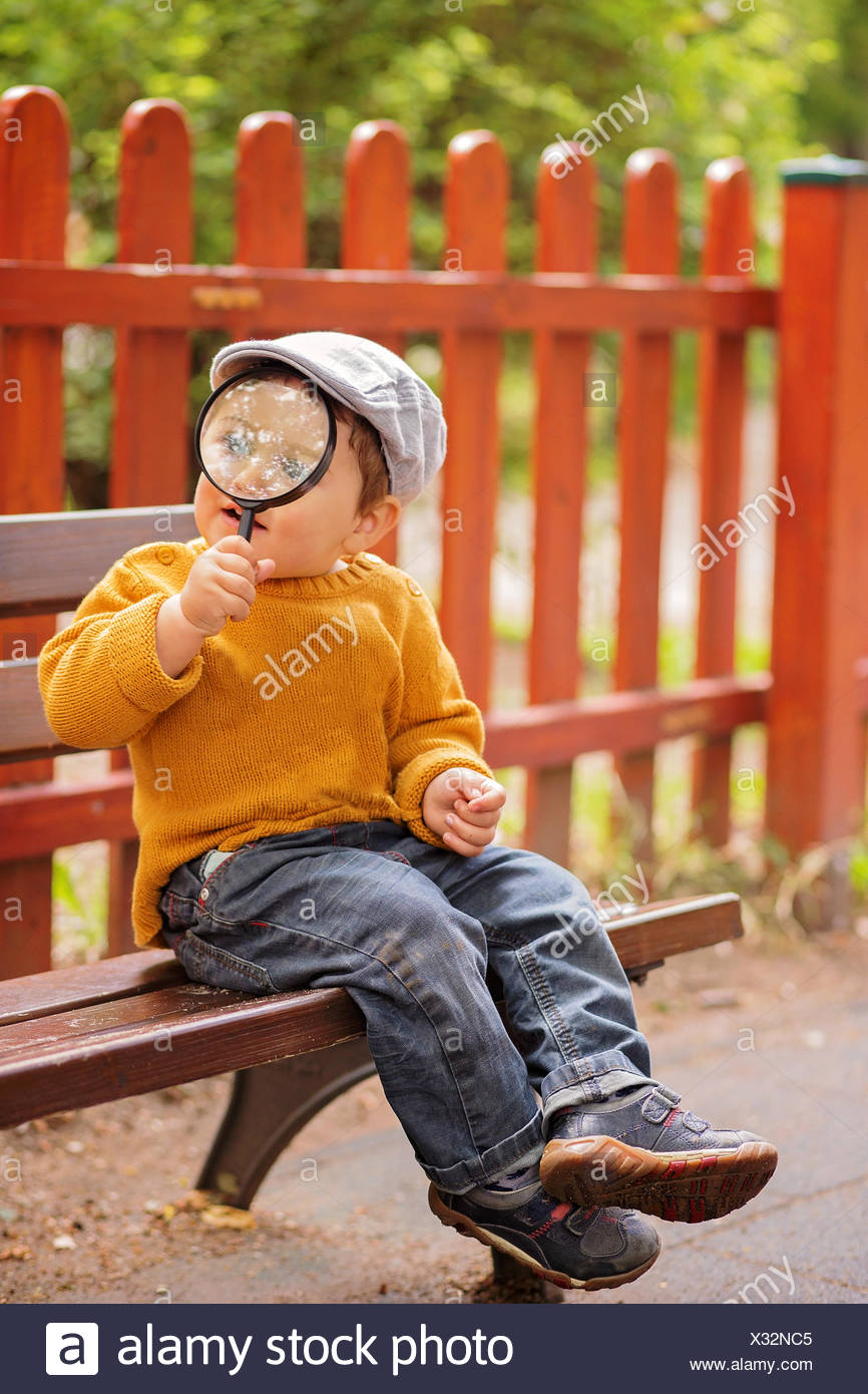 Boy Sitting On Bench Holding A Magnifying Glass Stock Photo