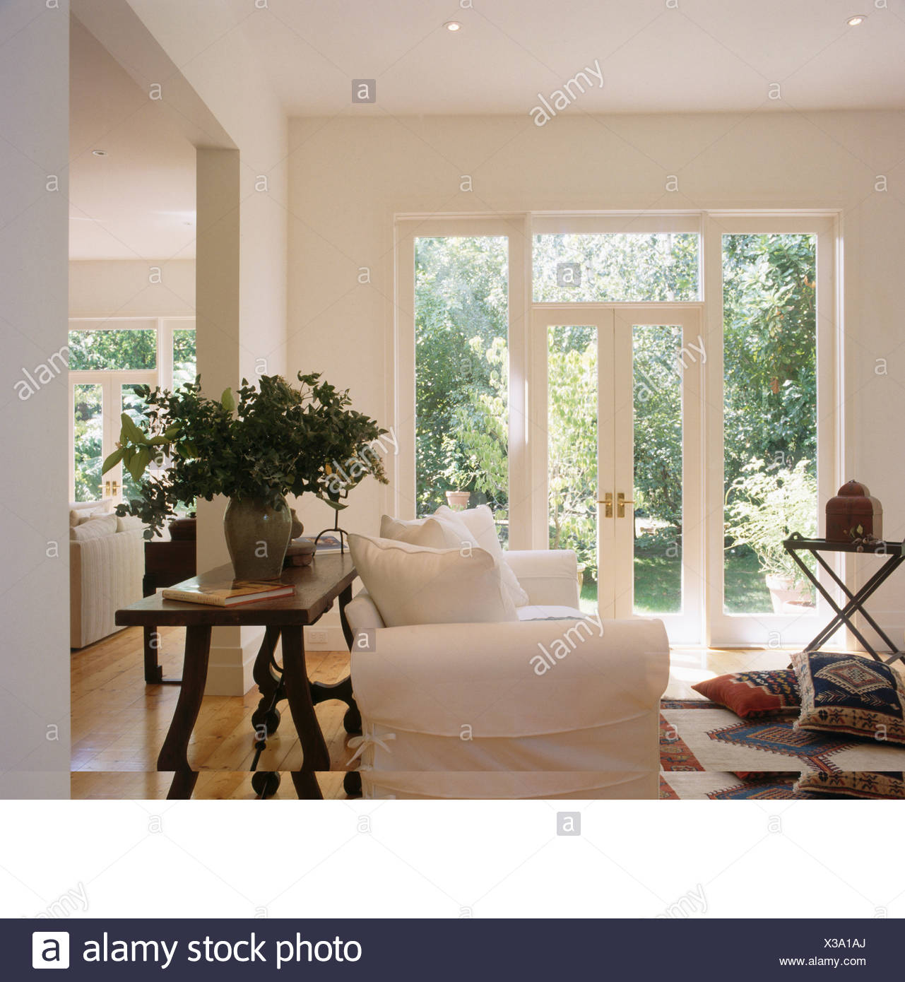 Tall Vase Of Flowers On Antique Table Behind White Sofa In Modern