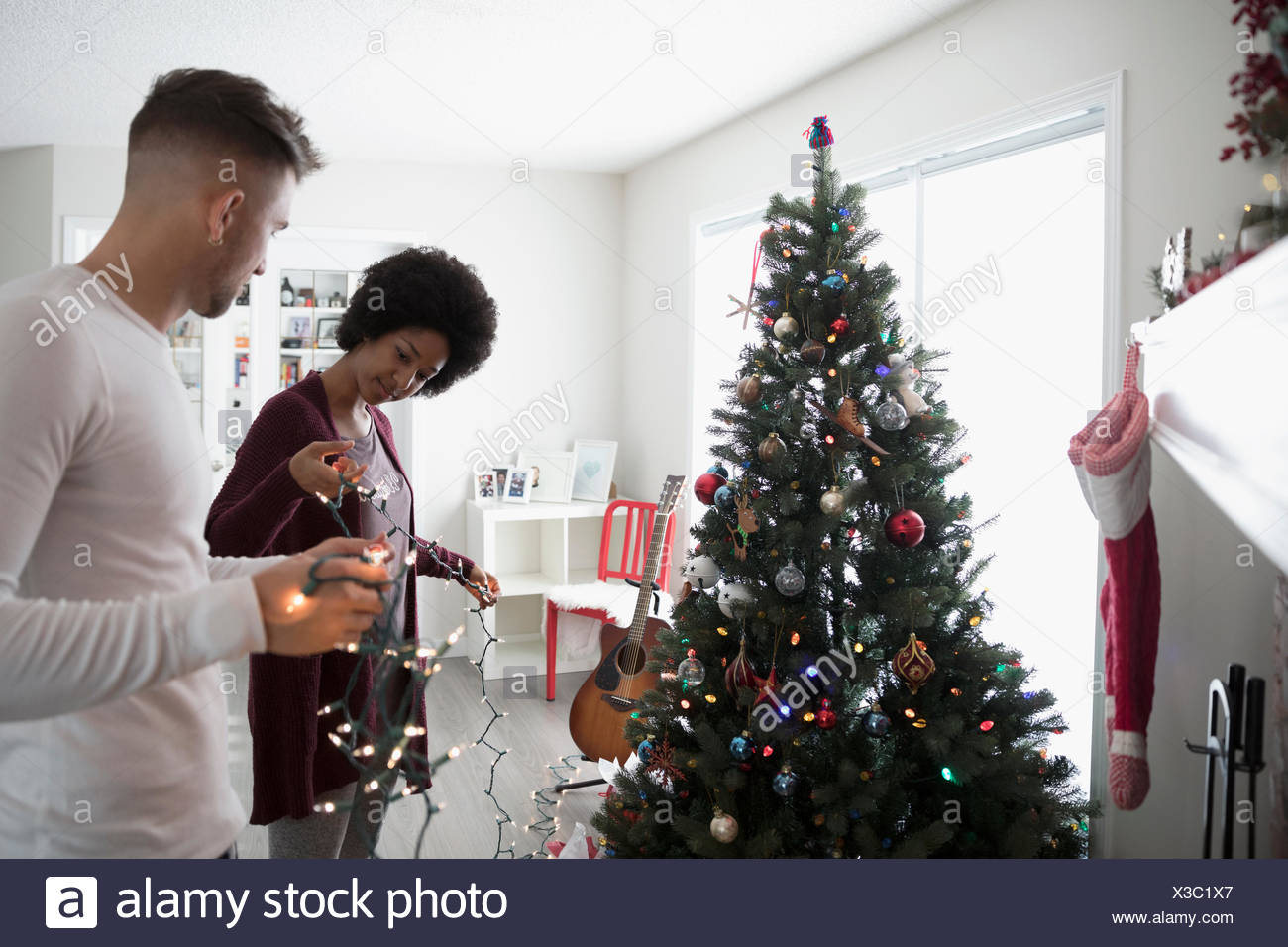 Young Couple Decorating Hanging Christmas Lights On Tree In