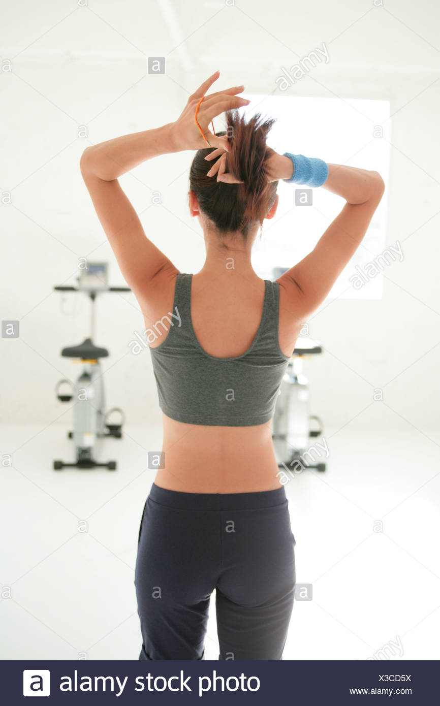 Young Woman Tying Hair Back In Gym Rear View Stock Photo