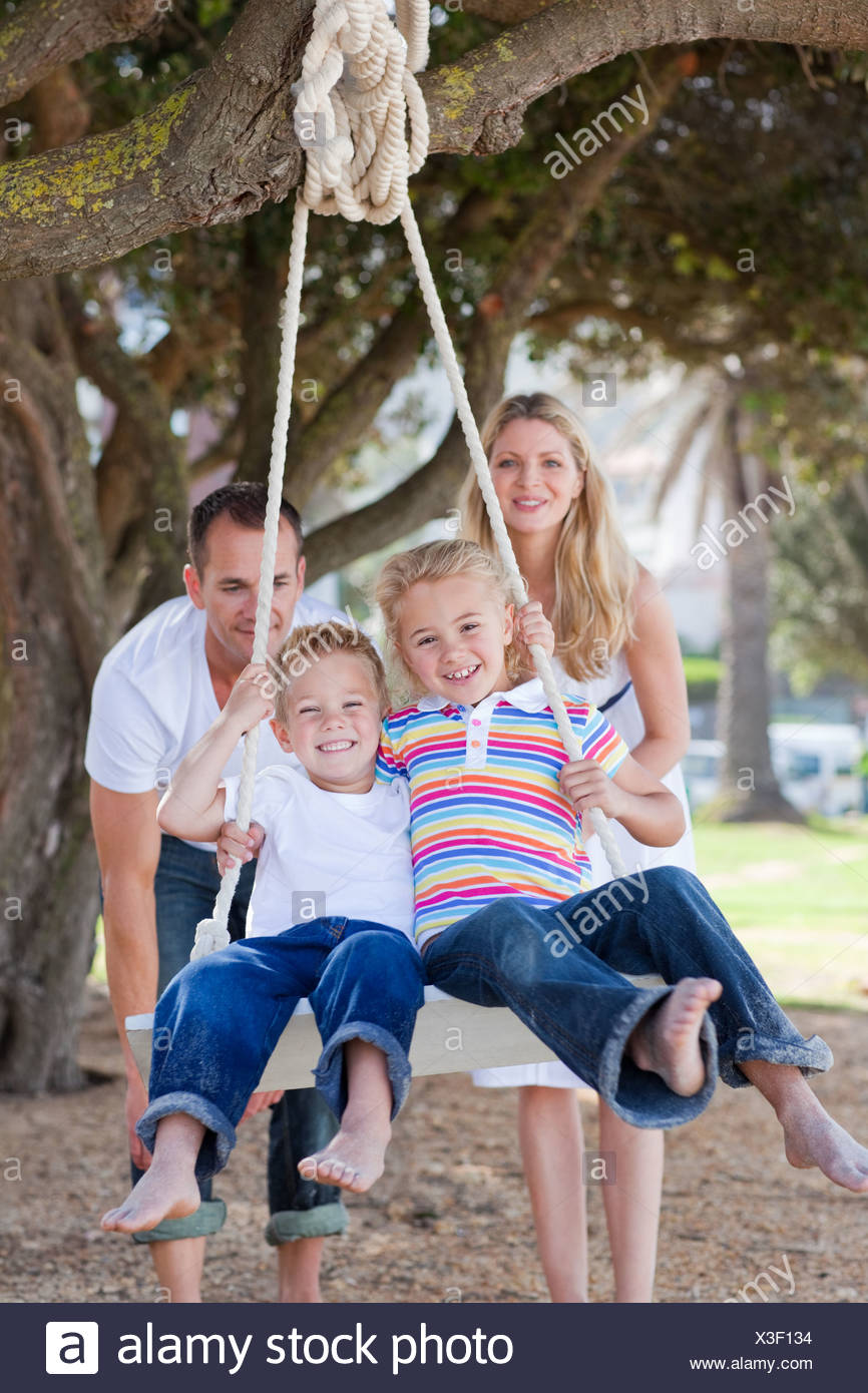 Joyful Parents Pushing Their Children On A Swing Stock Photo Alamy