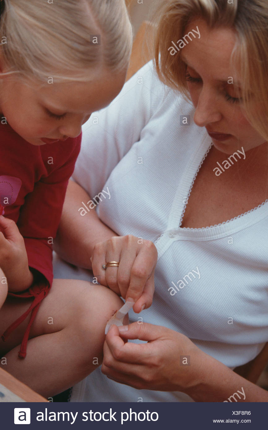 Mother With Long Blonde Hair Putting Plaster On Knee Of Female