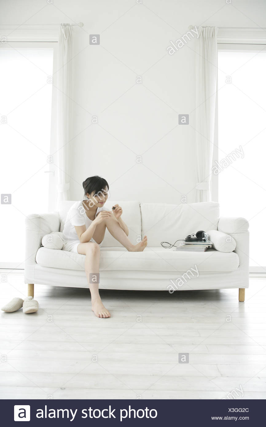 Young Woman Sitting On A Couch And Applying Nail Polish Stock